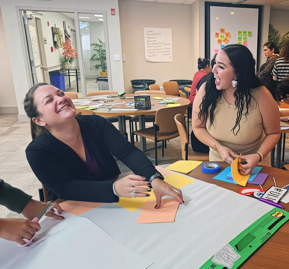 Two women laughing at a table with paper and markers
